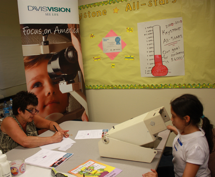 A child receives screening assistance from Cambridge Eye Doctors employee Debbie Sica during Davis Vision&rsquo;s recent vision screening at the Gerald and Darlene Jordan Club in Chelsea.
